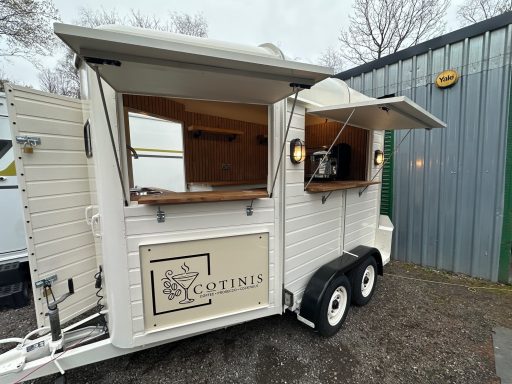 A white vintage-style food trailer with open serving windows and wooden counters.